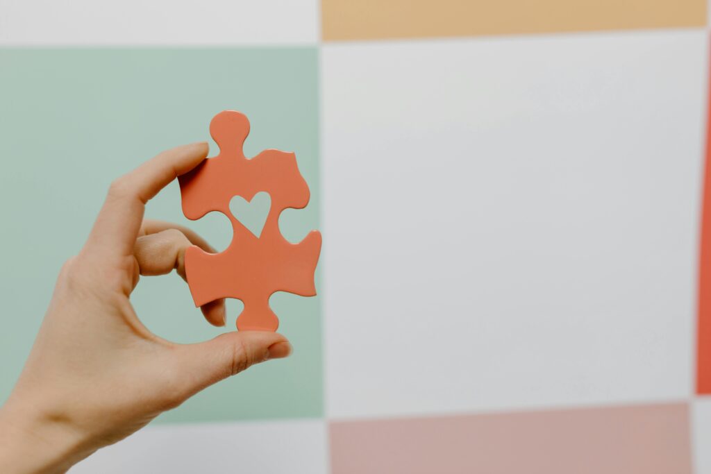 pexels-photo-8386182-8386182 Close-up of a hand holding a heart-shaped puzzle piece against a colorful background.